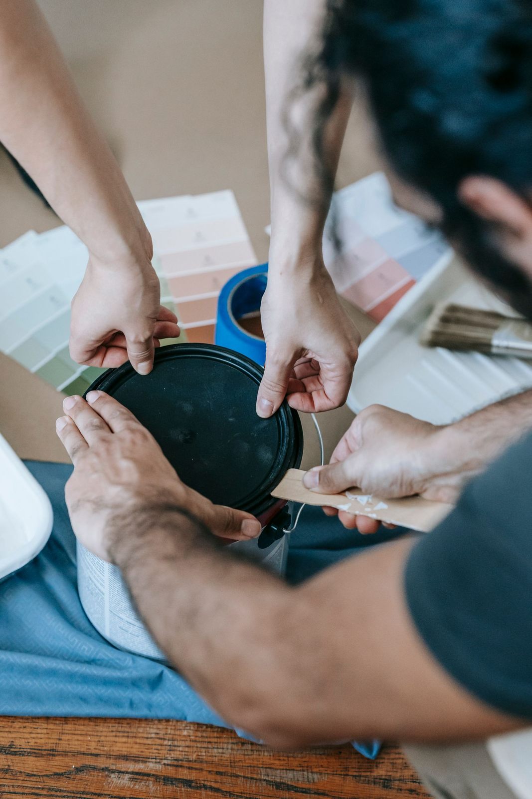 Two people collaborating on a home renovation project, opening a paint can with color swatches nearby