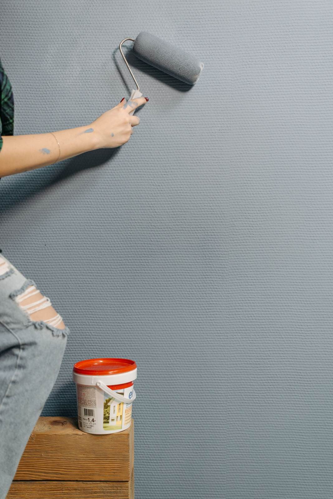 An adult painting a textured wall with a paint roller during home renovation